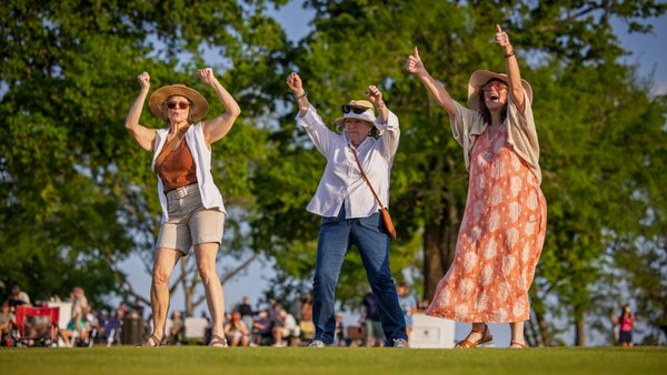 Three friends in sun hats dancing on the lawn at an outdoor concert